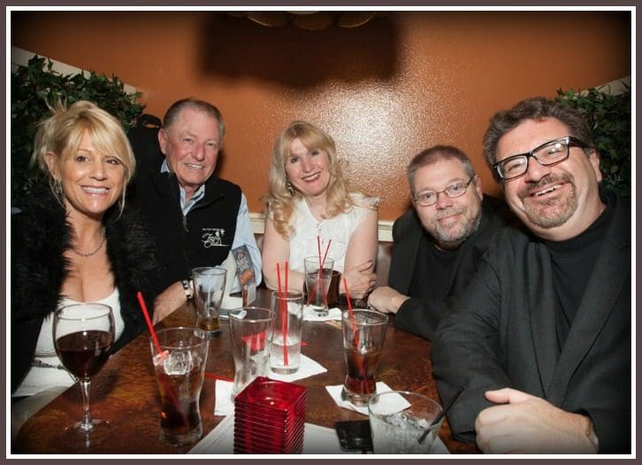 A Group of People Seated Around a Restaurant Table With Drinks, Including Glasses of Red Wine and Soda With Straws, in a Warmly Lit Room.