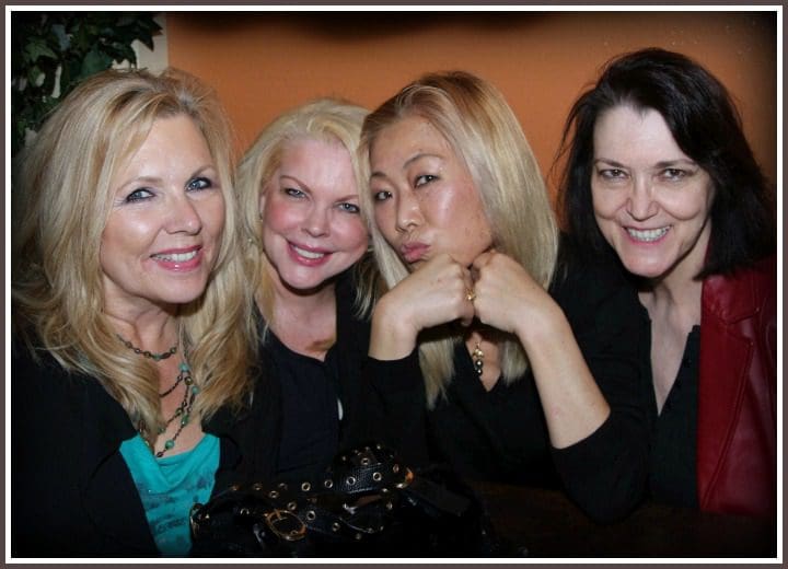 Four Individuals Sitting Side by Side with Varying Hairstyles and Attire, Such as Blonde Hair and Black Clothing, Against an Orange Background.